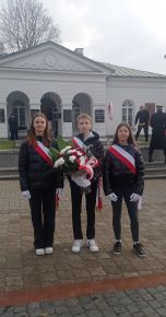Troje uczniów naszej szkoły z biało-czerwonymi kwiatami na tle Grobu Nieznanego Żołnierza podczas uroczystości z okazji Święta Niepodległości